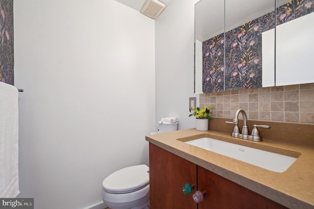 half bath with backsplash, toilet, and vanity