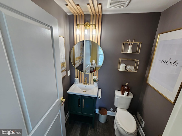 half bath featuring visible vents, toilet, vanity, wood finished floors, and baseboards