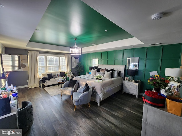 bedroom featuring a notable chandelier, a decorative wall, dark wood-style flooring, visible vents, and a raised ceiling