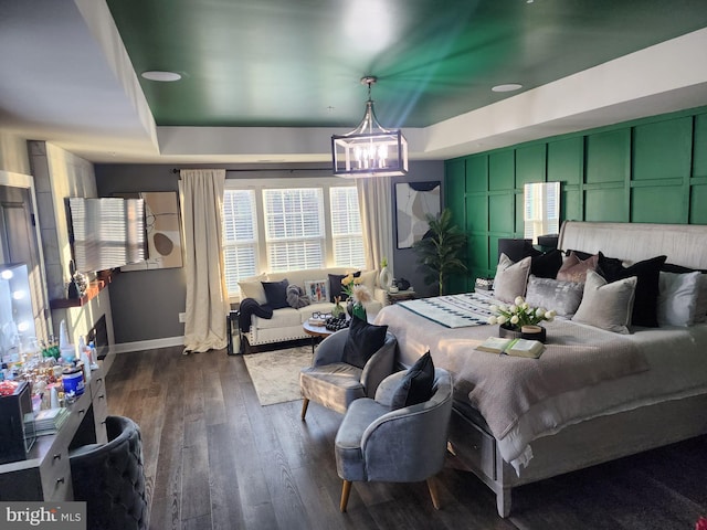 bedroom with a chandelier, a decorative wall, dark wood-type flooring, baseboards, and a raised ceiling