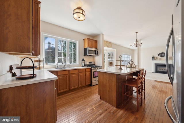 kitchen featuring a fireplace, light countertops, light wood-style flooring, appliances with stainless steel finishes, and a kitchen breakfast bar