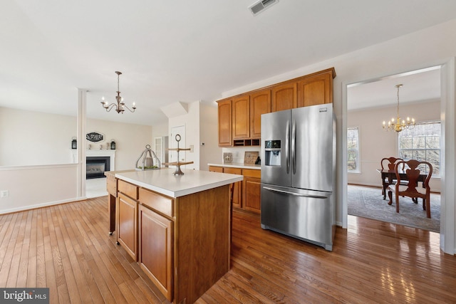 kitchen featuring a notable chandelier, a fireplace, stainless steel fridge with ice dispenser, light countertops, and brown cabinets