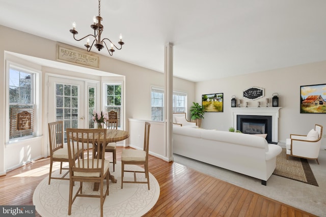 dining space featuring a glass covered fireplace, light wood-style flooring, baseboards, and an inviting chandelier