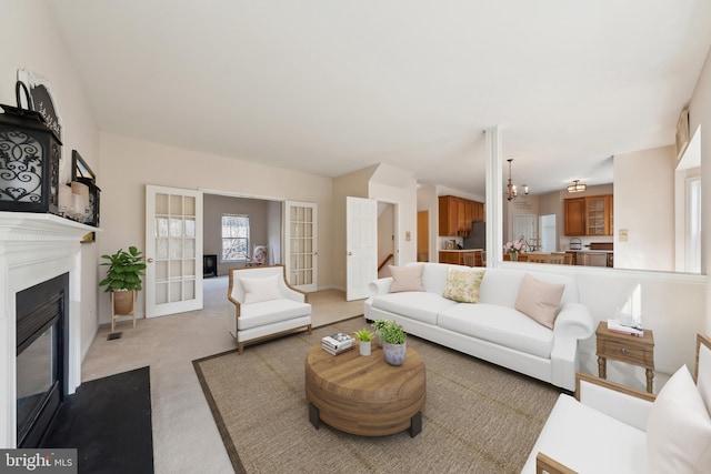 living room featuring carpet floors, a fireplace with flush hearth, baseboards, and a notable chandelier