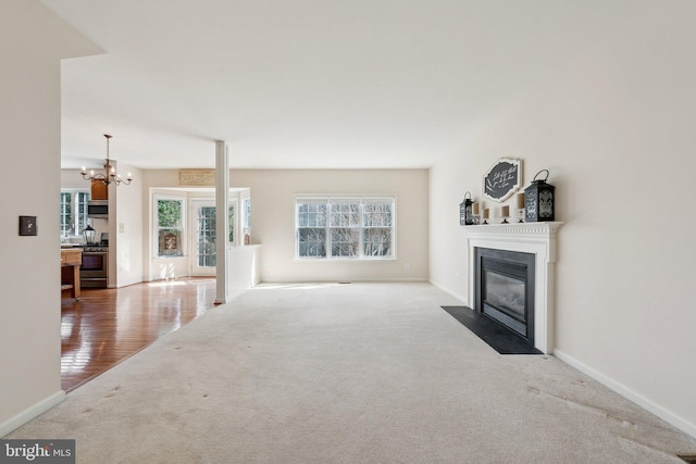 unfurnished living room featuring a chandelier, carpet, a fireplace with flush hearth, and baseboards