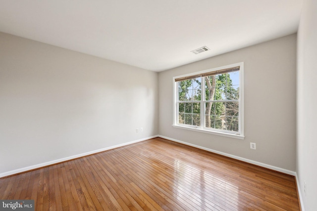 empty room featuring wood-type flooring, visible vents, and baseboards