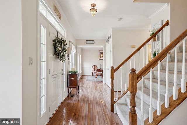 entryway featuring wood-type flooring, crown molding, and stairs