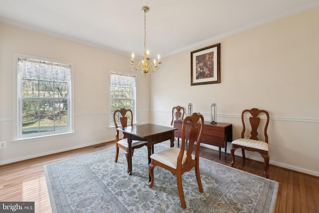 dining room featuring crown molding, visible vents, an inviting chandelier, baseboards, and hardwood / wood-style flooring