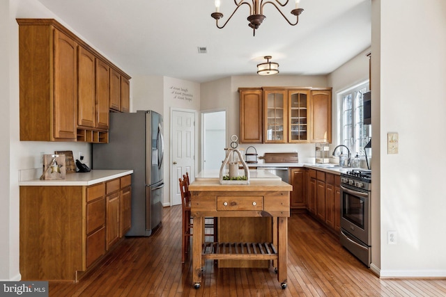 kitchen with light countertops, appliances with stainless steel finishes, a center island, dark wood-style floors, and glass insert cabinets