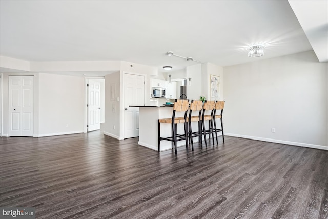 kitchen featuring dark wood-style flooring, stainless steel microwave, a peninsula, and a breakfast bar area