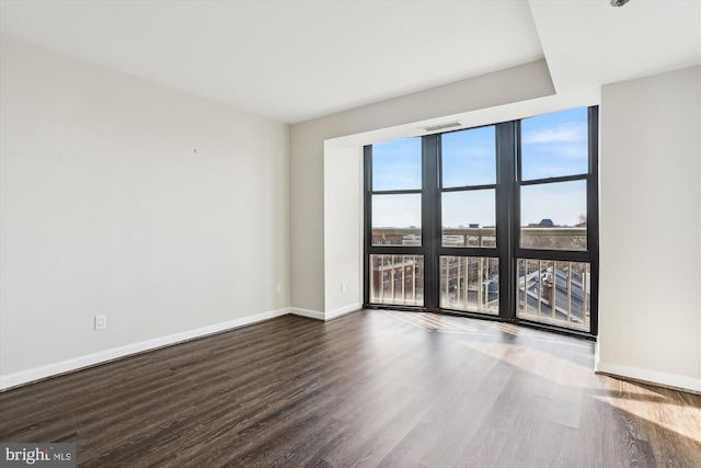 empty room with visible vents, floor to ceiling windows, baseboards, and wood finished floors