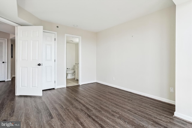 unfurnished bedroom featuring dark wood-style floors, ensuite bath, and baseboards