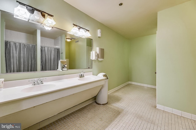 full bath featuring double vanity, a sink, baseboards, and tile patterned floors