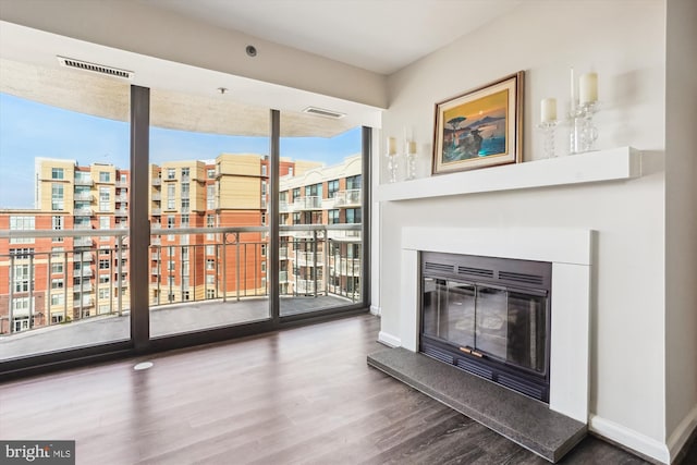 unfurnished living room featuring baseboards, visible vents, wood finished floors, and a glass covered fireplace