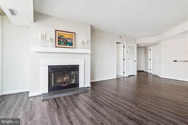 unfurnished living room with baseboards, visible vents, wood finished floors, and a glass covered fireplace