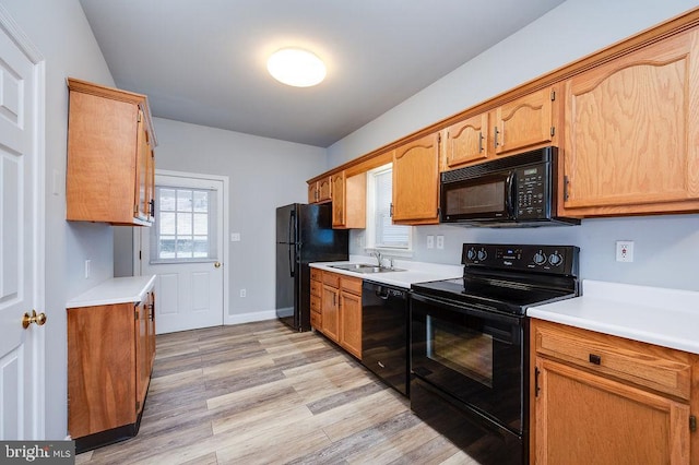 kitchen featuring black appliances, light wood finished floors, a sink, and light countertops