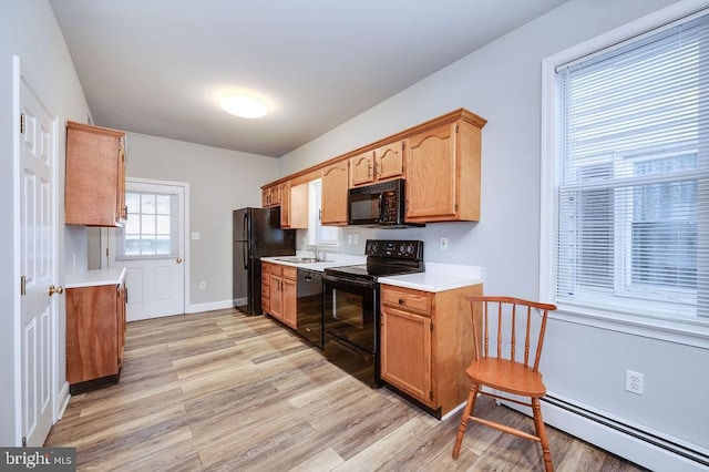 kitchen featuring light wood finished floors, a baseboard radiator, light countertops, a sink, and black appliances