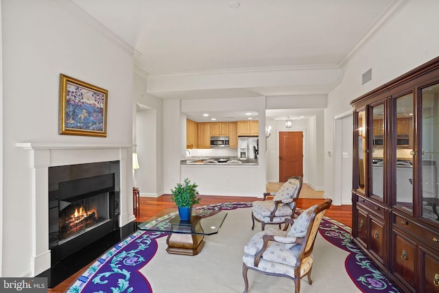 living area featuring visible vents, ornamental molding, a warm lit fireplace, and wood finished floors