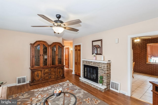 living area featuring visible vents, a fireplace, brick wall, and wood finished floors