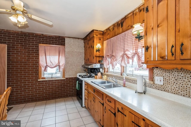 kitchen with range with gas stovetop, brick wall, a sink, light countertops, and brown cabinets