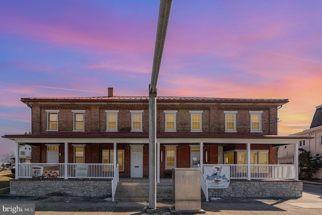 multi unit property with covered porch, brick siding, and a chimney