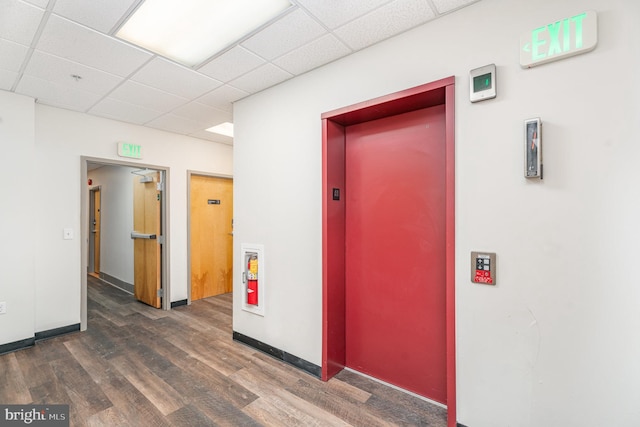 hall with baseboards, dark wood-type flooring, a drop ceiling, and elevator