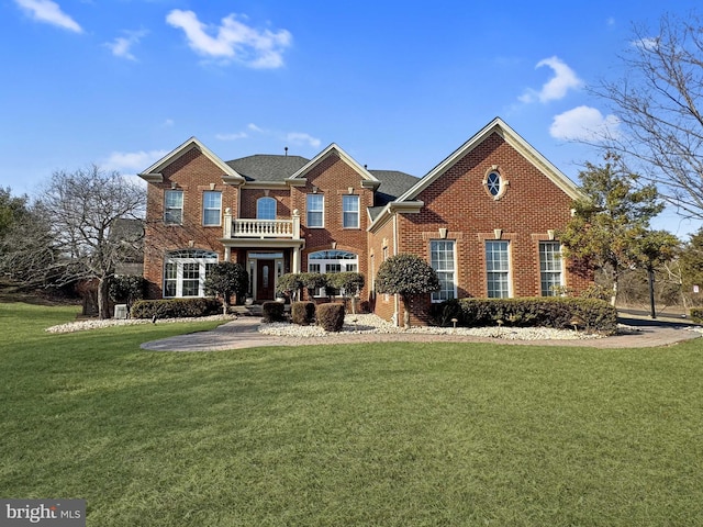 colonial home with a balcony, a front yard, and brick siding