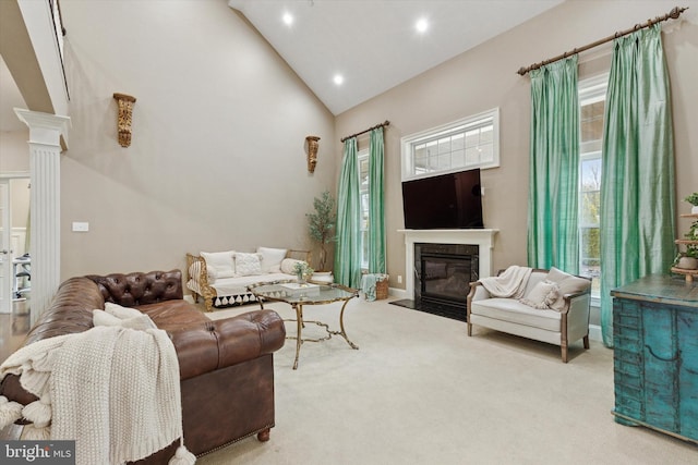 carpeted living area with high vaulted ceiling, a fireplace with flush hearth, decorative columns, and recessed lighting