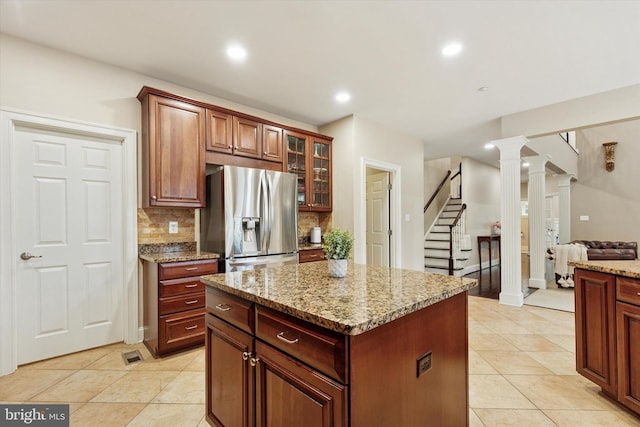 kitchen with decorative columns, tasteful backsplash, glass insert cabinets, light stone countertops, and stainless steel fridge