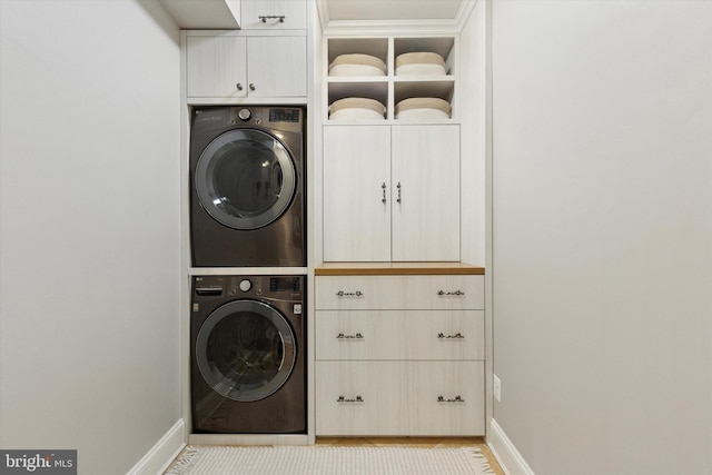 laundry room featuring cabinet space, baseboards, and stacked washer and dryer