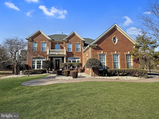 colonial inspired home featuring a balcony, a front yard, and brick siding