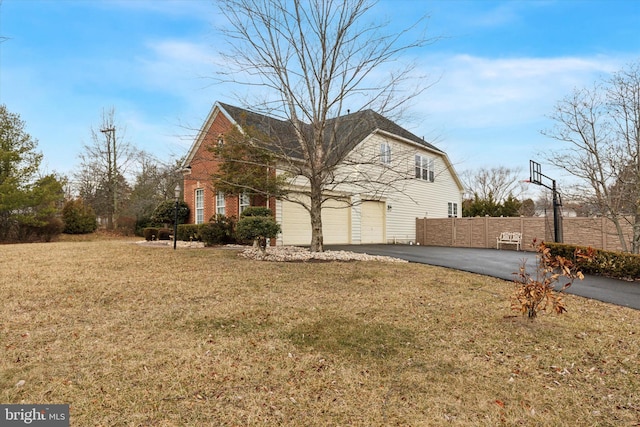 view of side of home with aphalt driveway, a garage, brick siding, fence, and a yard