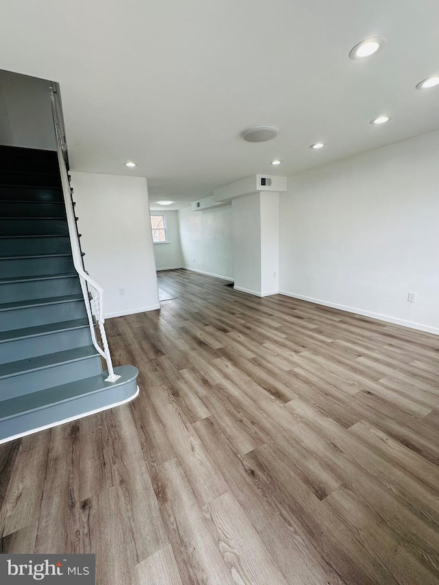 unfurnished living room featuring light wood-type flooring, stairway, baseboards, and recessed lighting