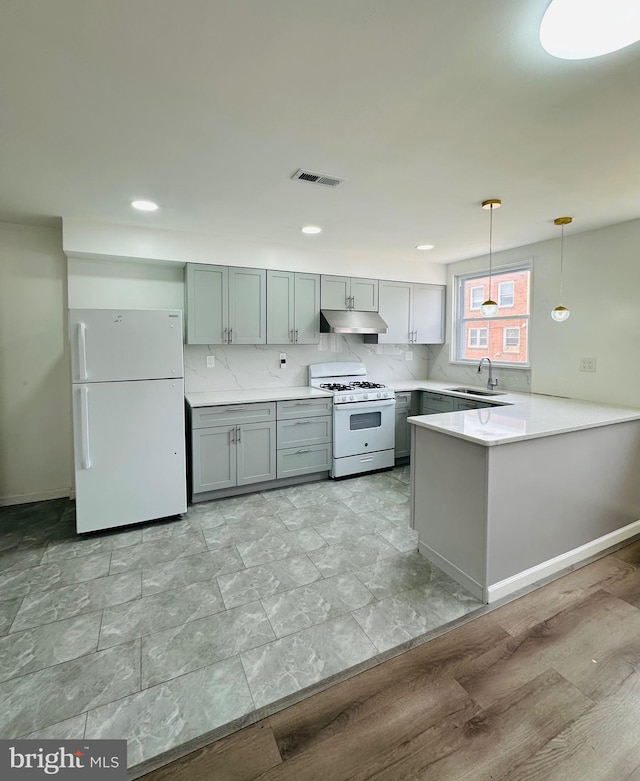 kitchen featuring a peninsula, white appliances, a sink, light countertops, and pendant lighting