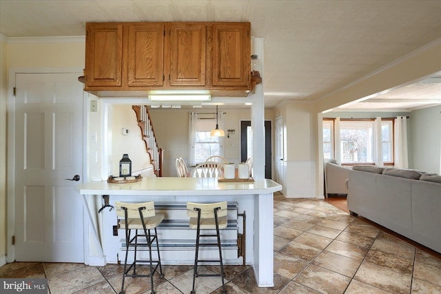 kitchen featuring brown cabinets, crown molding, open floor plan, a peninsula, and a kitchen breakfast bar