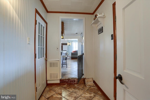 corridor with light tile patterned floors, radiator heating unit, baseboards, and crown molding