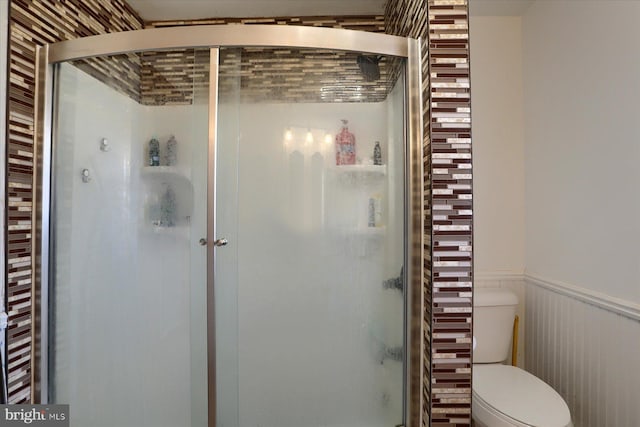 bathroom with wainscoting, a shower stall, and toilet