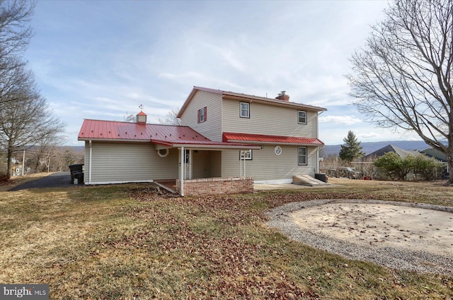 back of property featuring a patio, metal roof, a chimney, and a lawn