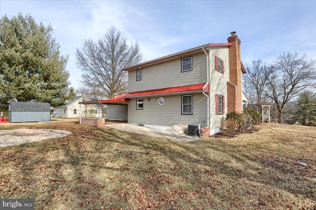 back of house with a chimney, a lawn, central AC, and an outdoor structure