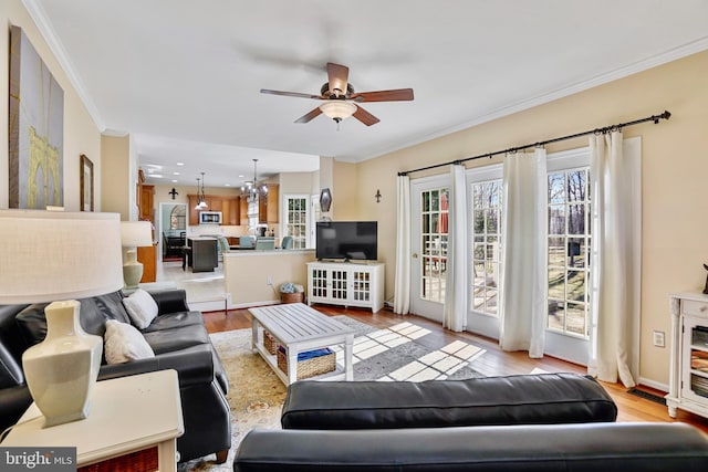 living area with ornamental molding, light wood-type flooring, baseboards, and ceiling fan with notable chandelier