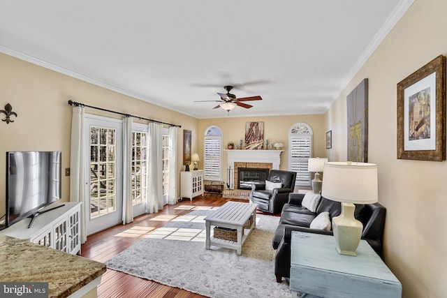 living area featuring wood-type flooring, a fireplace, ornamental molding, and ceiling fan