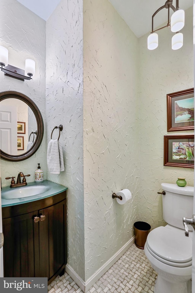 bathroom with a textured wall, vanity, toilet, and baseboards