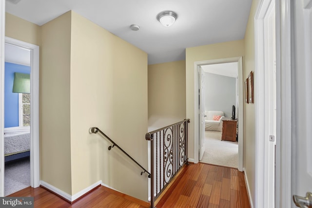 corridor with baseboards, wood finished floors, and an upstairs landing