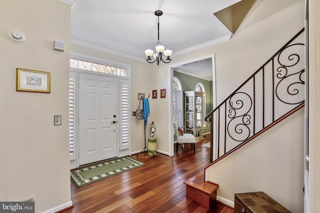 foyer entrance with baseboards, stairway, ornamental molding, hardwood / wood-style floors, and an inviting chandelier