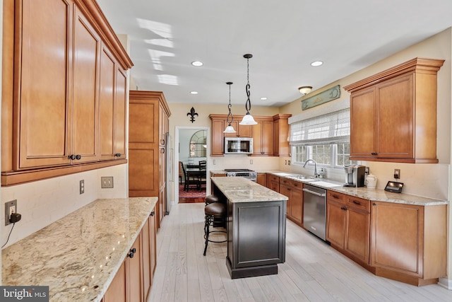 kitchen with light stone counters, a breakfast bar, a sink, appliances with stainless steel finishes, and light wood finished floors