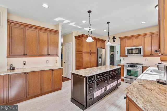 kitchen featuring stainless steel appliances, light stone counters, decorative light fixtures, and light wood-style floors