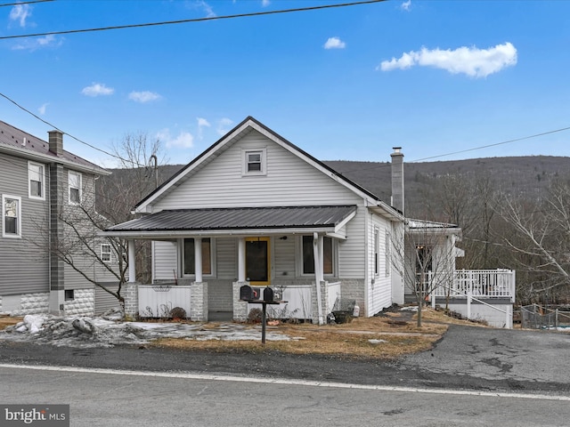 view of front of property featuring metal roof, a chimney, and a porch