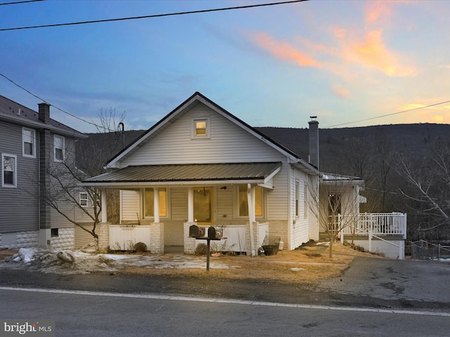 bungalow-style house featuring metal roof, a chimney, and a porch