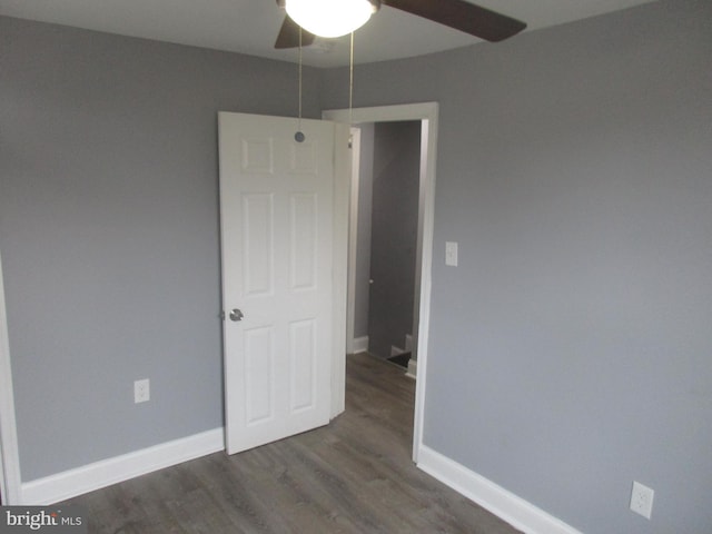 unfurnished bedroom featuring dark wood-type flooring, a ceiling fan, and baseboards