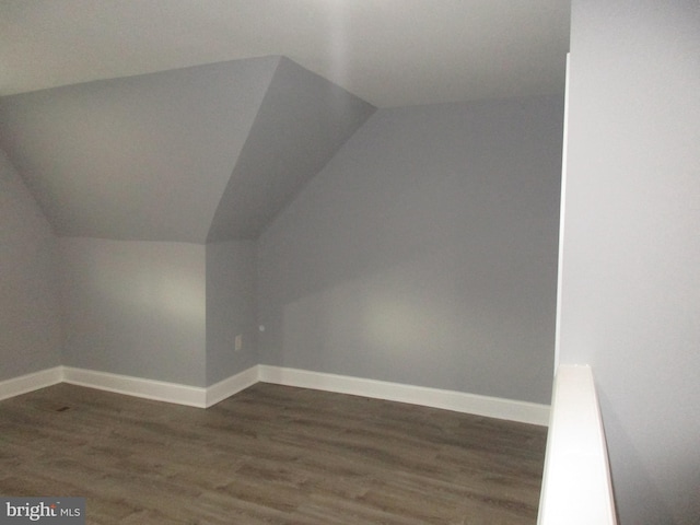 additional living space featuring vaulted ceiling, dark wood-style flooring, and baseboards